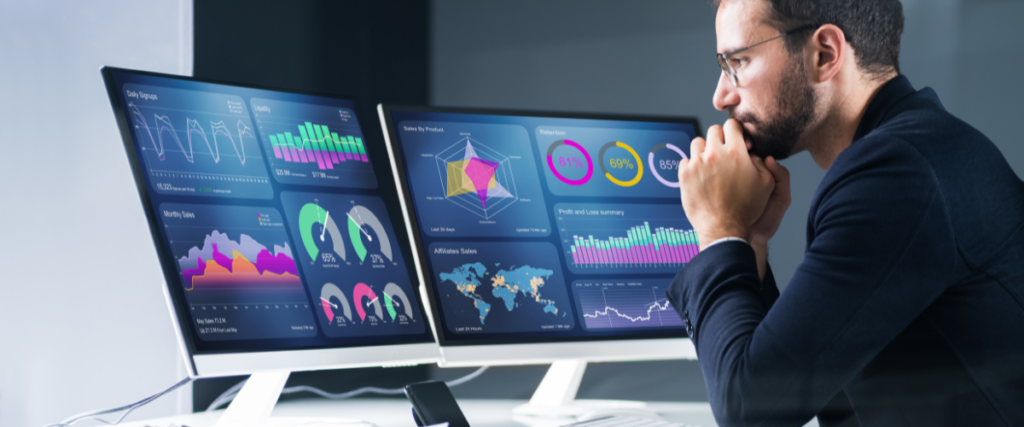 man at desk looking at monitors with data presented in graphs